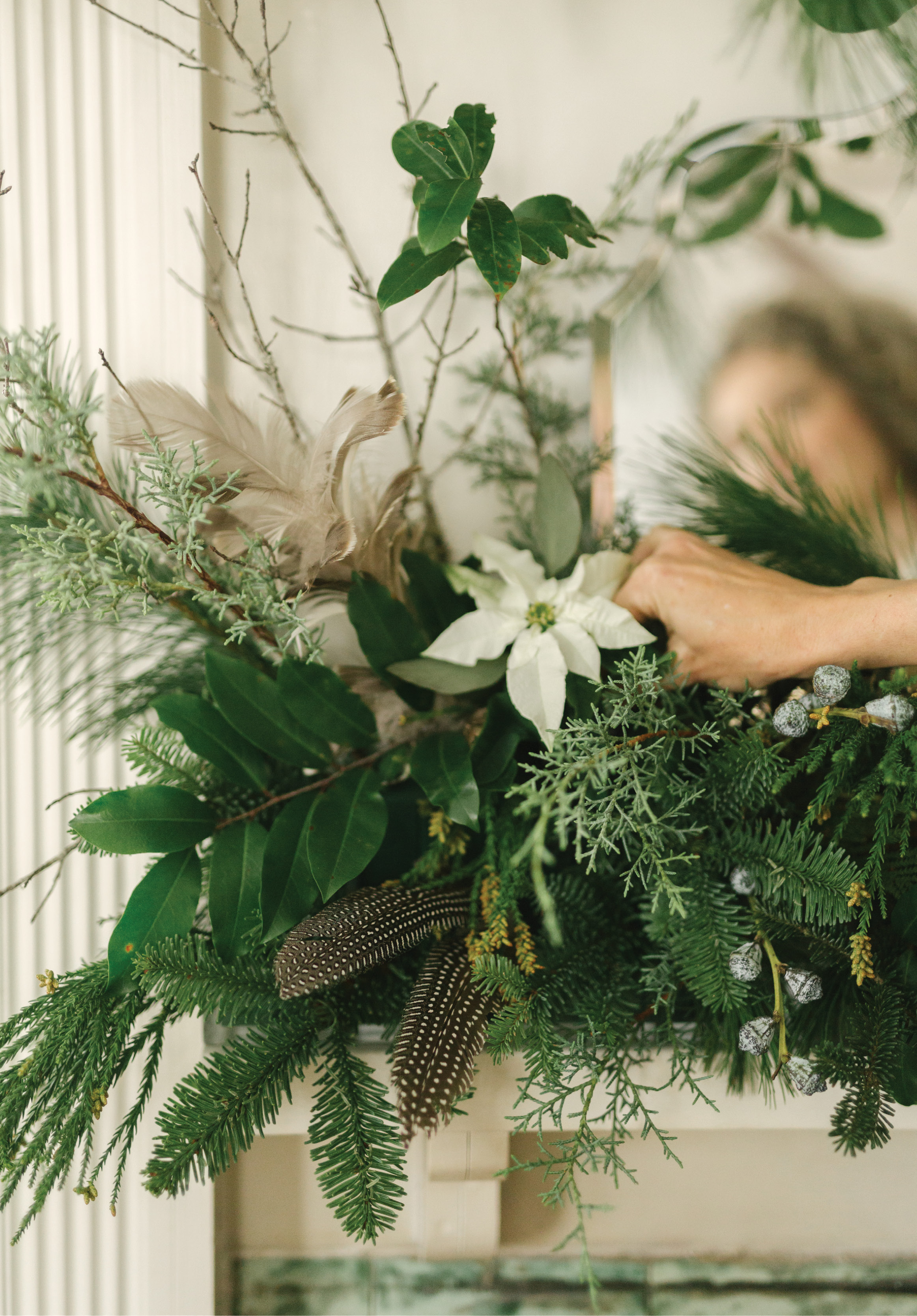 For her dramatic mantelpiece, she fills narrow Lucite trays with floral foam, then a mix of greens plus branches covered in lichen, silver-hued Cecropia leaves, and guinea hen feathers for tons of texture and a woodsy feel.