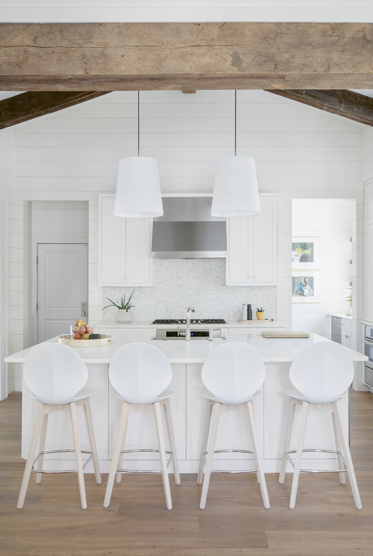 In the streamlined kitchen, seamless cabinetry on each side of the expansive marble-topped island holds everything from cookware to craft supplies, as well as a built-in beverage cooler for kids’ drinks. To the right of the chevron-tiled backsplash, a walk-in pantry houses cooking staples and the wine bar.