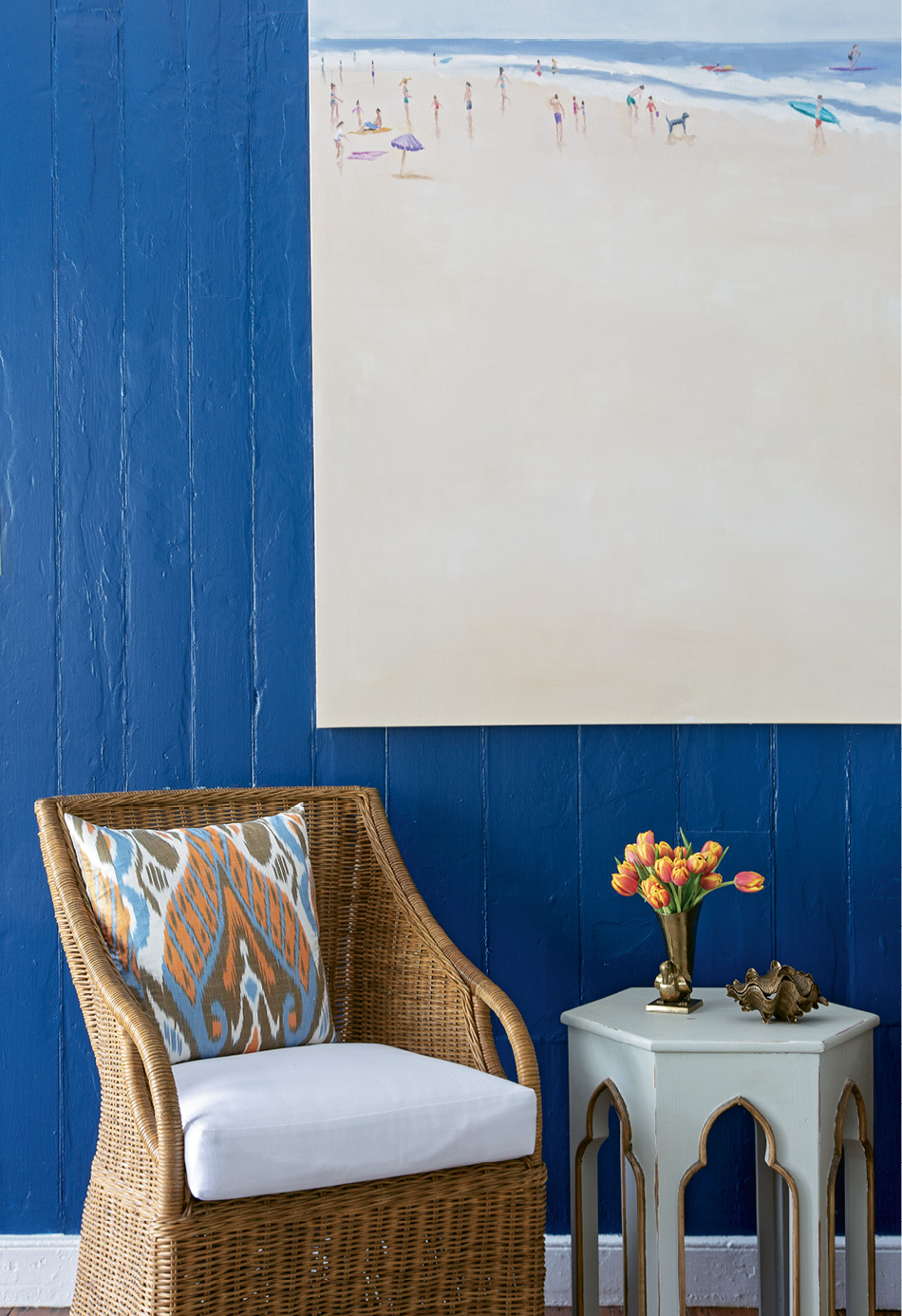 Serene Scene: Local artist Shannon Wood’s expansive beach scene positively pops from the bold blue walls, a cheery welcome to the home. Beneath it, a Williams-Sonoma Home wicker chair invites visitors to sit and stay awhile.