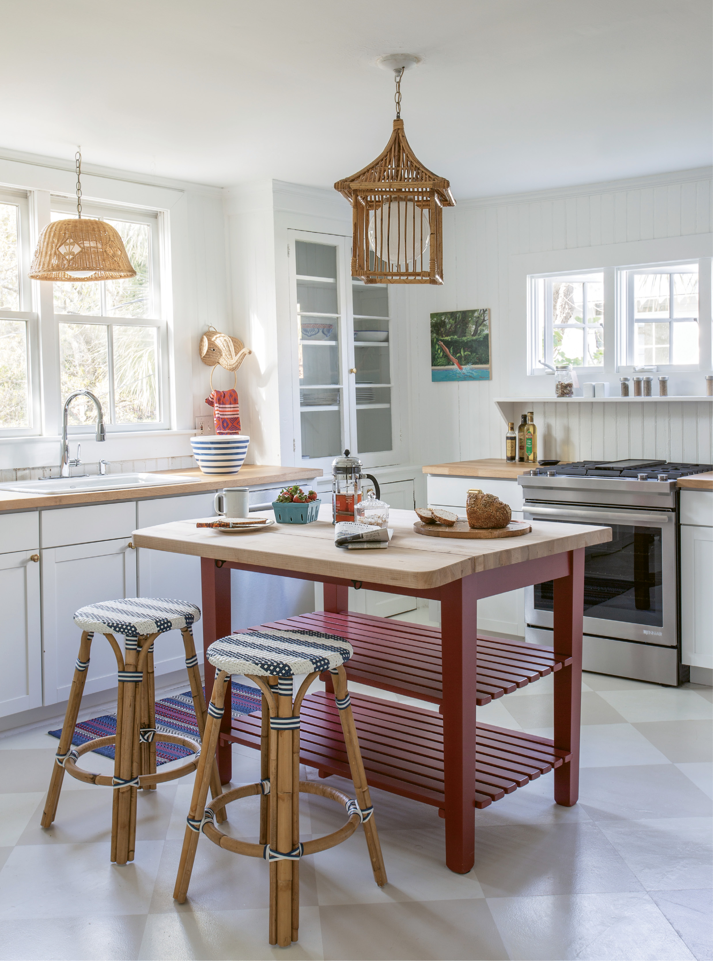 Gather ’Round: Working around the original glass-fronted cabinets in the kitchen, Isbell added a butcher-block island to allow for flexible seating in the space. On the floor, a chessboard pattern painted by Suzanne Allen Studio continues the theme of painted wood flooring seen throughout the home.