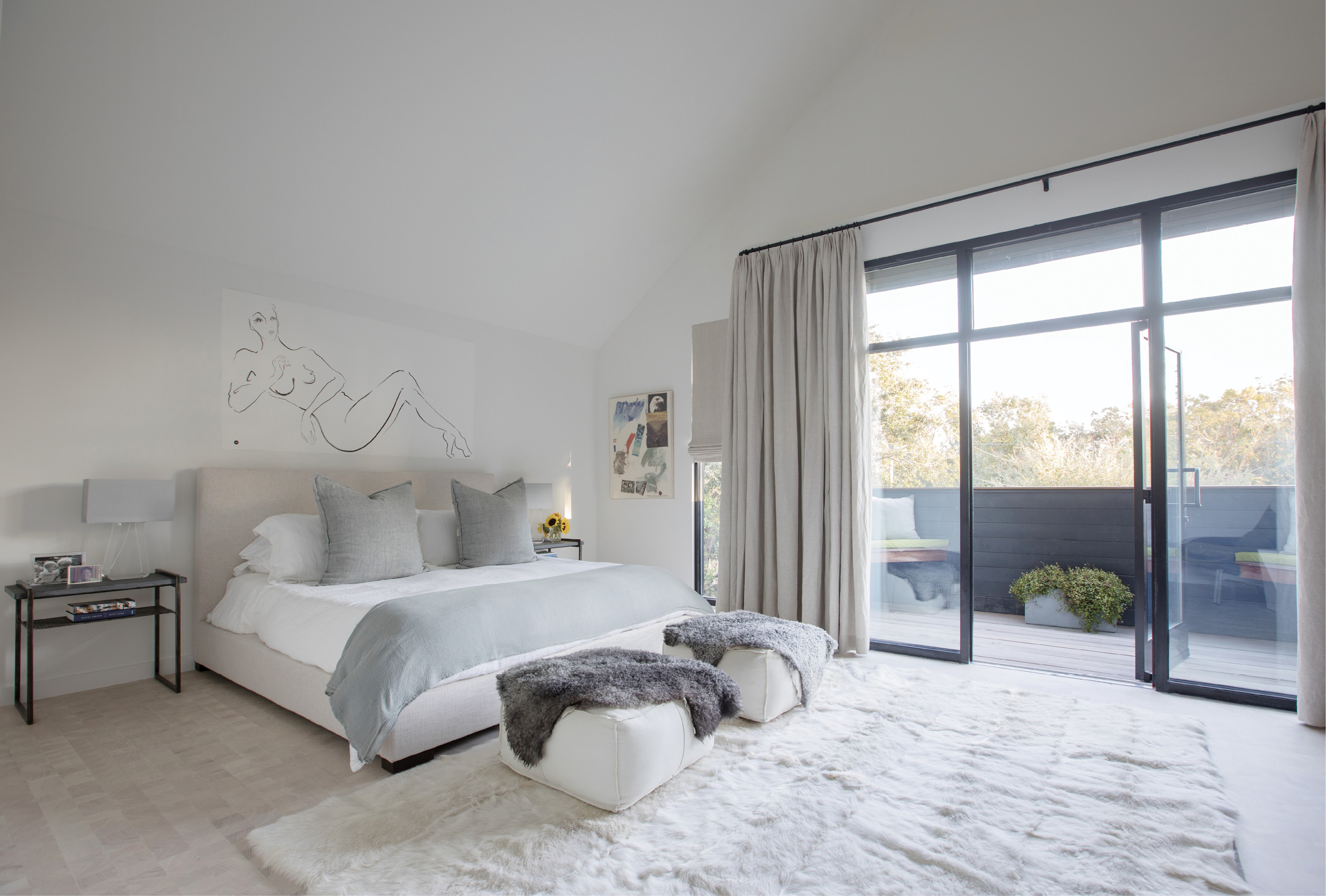 TREETOP RETREAT: The expansive, light-filled, second-floor master bedroom, located at the front of the house, boasts more floor-to-ceiling windows and a balcony with arboreal views. Natural linen drapery, also repeated from downstairs, helps block out the light when necessary; a drawing by Carrie Beth Waghorn watches over the scene.