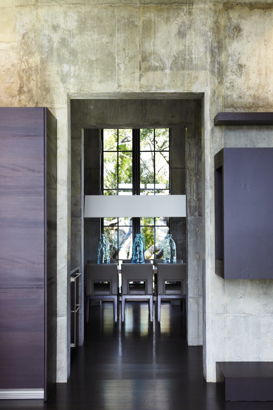 Dining In: Interior designer Paola Thomas chose a  bamboo dining table, leather-upholstered chairs, and a rectangular shade pendant for the dining room.  A collection of aqua glass bottles dresses up the  room’s neutral hues.