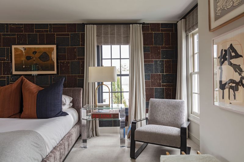 A dramatic Romo wallpaper frames the primary bedroom, complete with a velvet bed designed by Brown. Acrylic side tables topped by Judith Norman brass lamps and a retro lounge chair from Arteriors add glamour. The play of dark and light, texture and tone creates a cozy space while showcasing more of the couple’s artwork, including pieces by Jean Dubuffet, Tadeusz Lapinski, and Robert Motherwell.