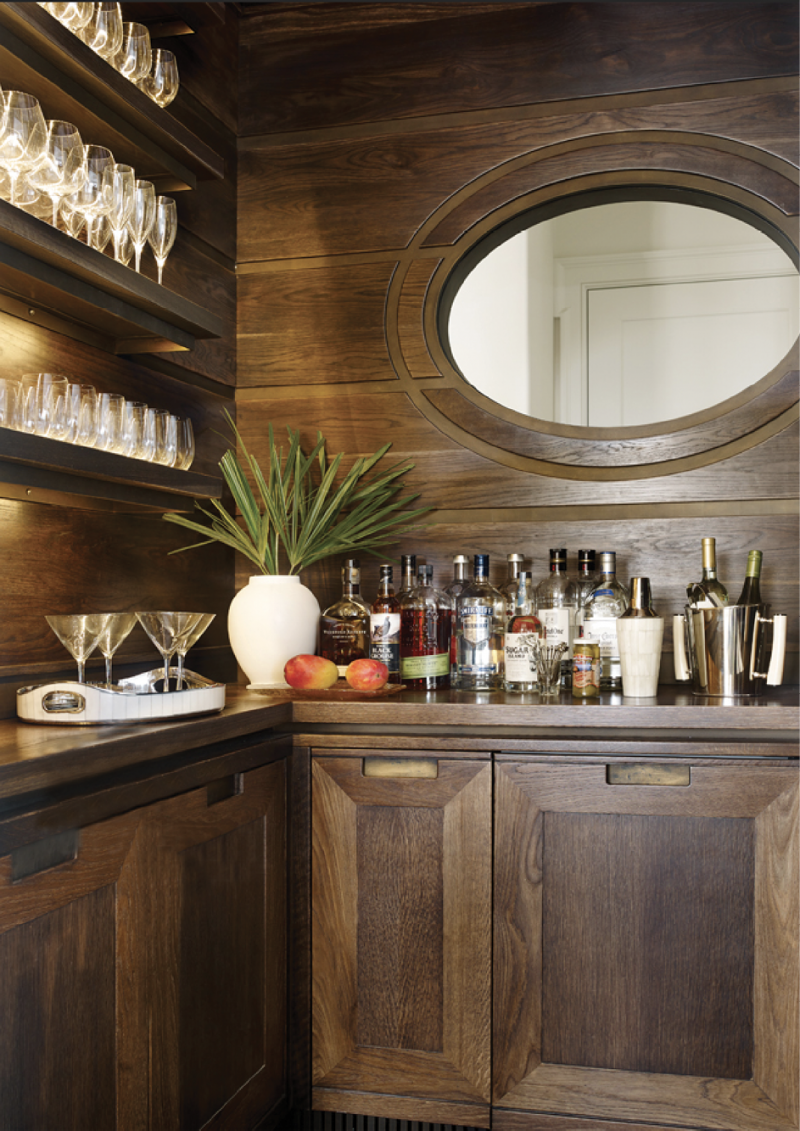 Handsome Hideaway - Custom cypress cabinetry by local firm ECR Joinery and an oval-shaped interior window distinguish this bar, which separates the kitchen and living room.  Location: Kiawah Island, (owned by Leah and Gee Aldridge) Issue: July 2018, “Style &amp; Substance”  Photographer: Emily Jenkins Followill