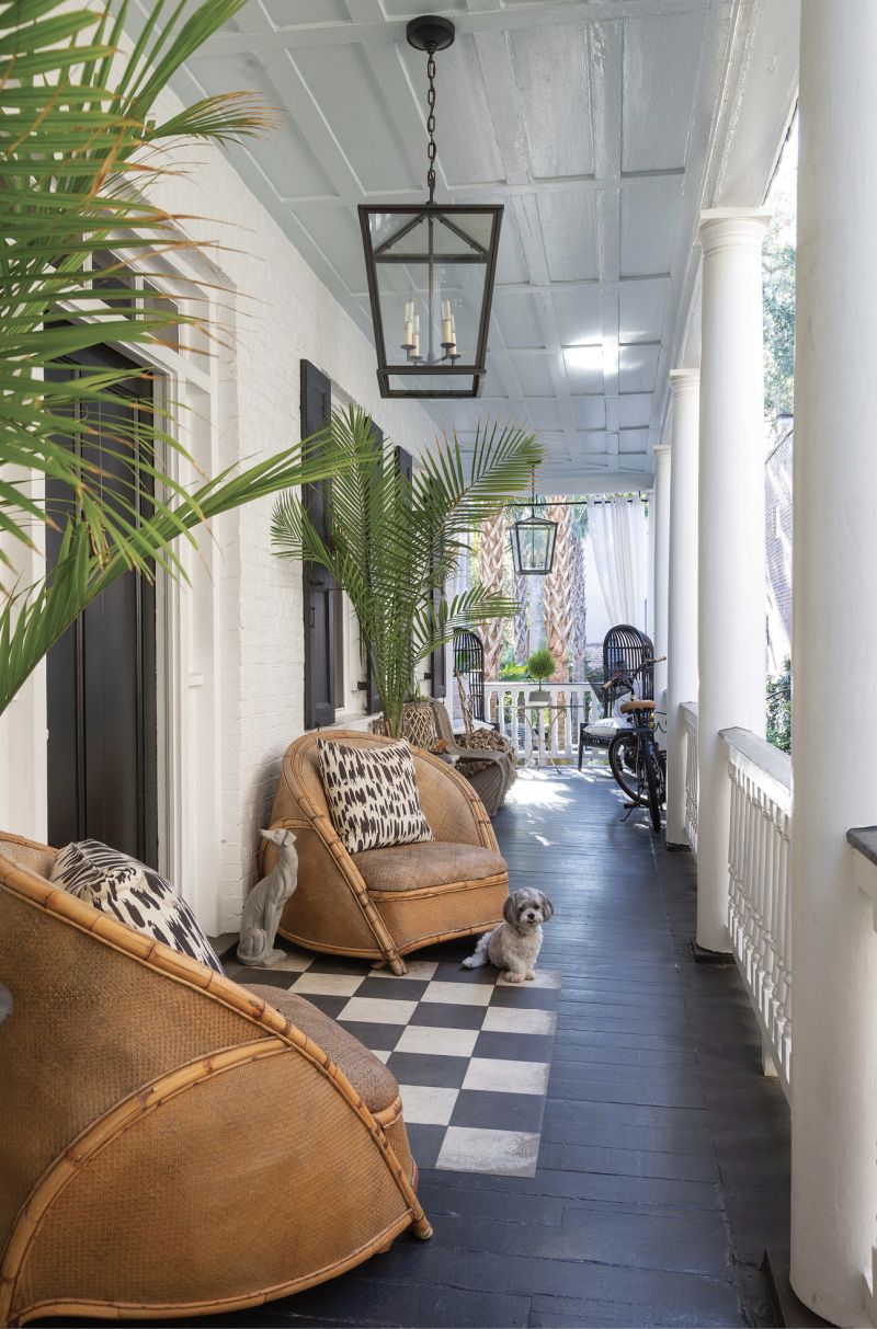 Old School Meets New - While the piazza floor of this circa-1840 Greek Revival single house is painted in traditional “Charleston green” and its ceiling the customary pale blue, the circa-1930s rattan chairs and bold patterned pillows hint at the blend of modern and vintage styles within.  Location: Ansonborough (owned by Betsy and Bruce Finley)  Issue: February 2020, “A Twist on Tradition”  Photographer: Julia Lynn
