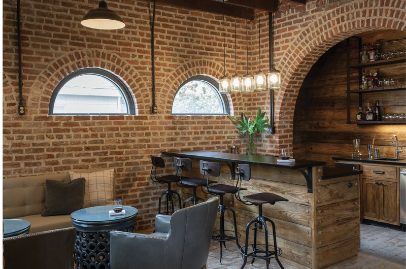 Encircle the Squares - Since arches dominate the ground floor of this carriage house, designer Kristin Peake echoed the motif with cylindrical side tables and pendant lights and round mirrors to soften the hard lines of the floor plan and exposed brickwork.  Location: South of Broad  (dependency of the Porcher-Simonds House, circa 1856, owned by Kristy and Rick Schultz)  Issue: September 2019,  “One Gorgeous Garage”  Photographer:  Julia Lynn