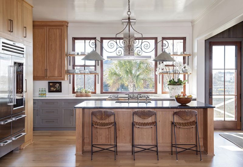 The adjoining kitchen continues the Gallic theme, where a 19th-century French wrought-iron chandelier with zinc shades from Golden &amp; Associates Antiques hangs over the soapstone countertop with a custom-coined edge. Three vintage 1950s rush-and-wood slat bar stools cozy up to the white oak island.