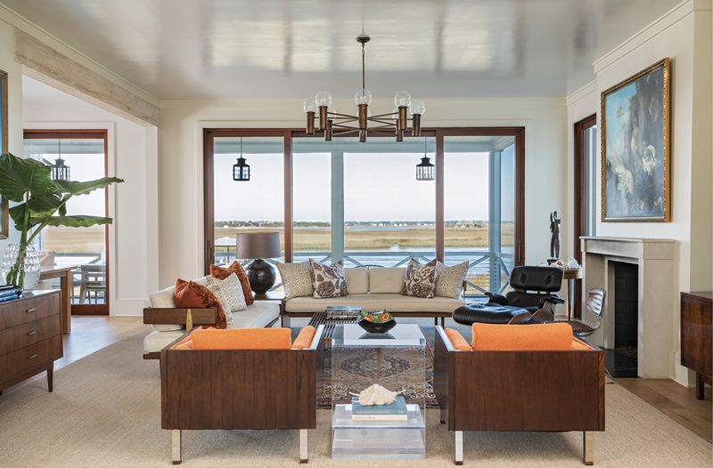 Clean Lines: The home’s interiors are designed for comfort with a hefty dose of style. Low, mid-century furniture, including a pair of circa-1960 Danish Brazilian rosewood “Cube” club chairs by Jydsk Møbelværk, a two-piece modern sectional by Harvey Probber, and an acrylic side table, draw the eye to the view beyond. The soft, marsh-inspired palette is highlighted by the custom Sherwin Williams faint blue semi-gloss paint on the ceiling, evoking the Lowcountry sky.