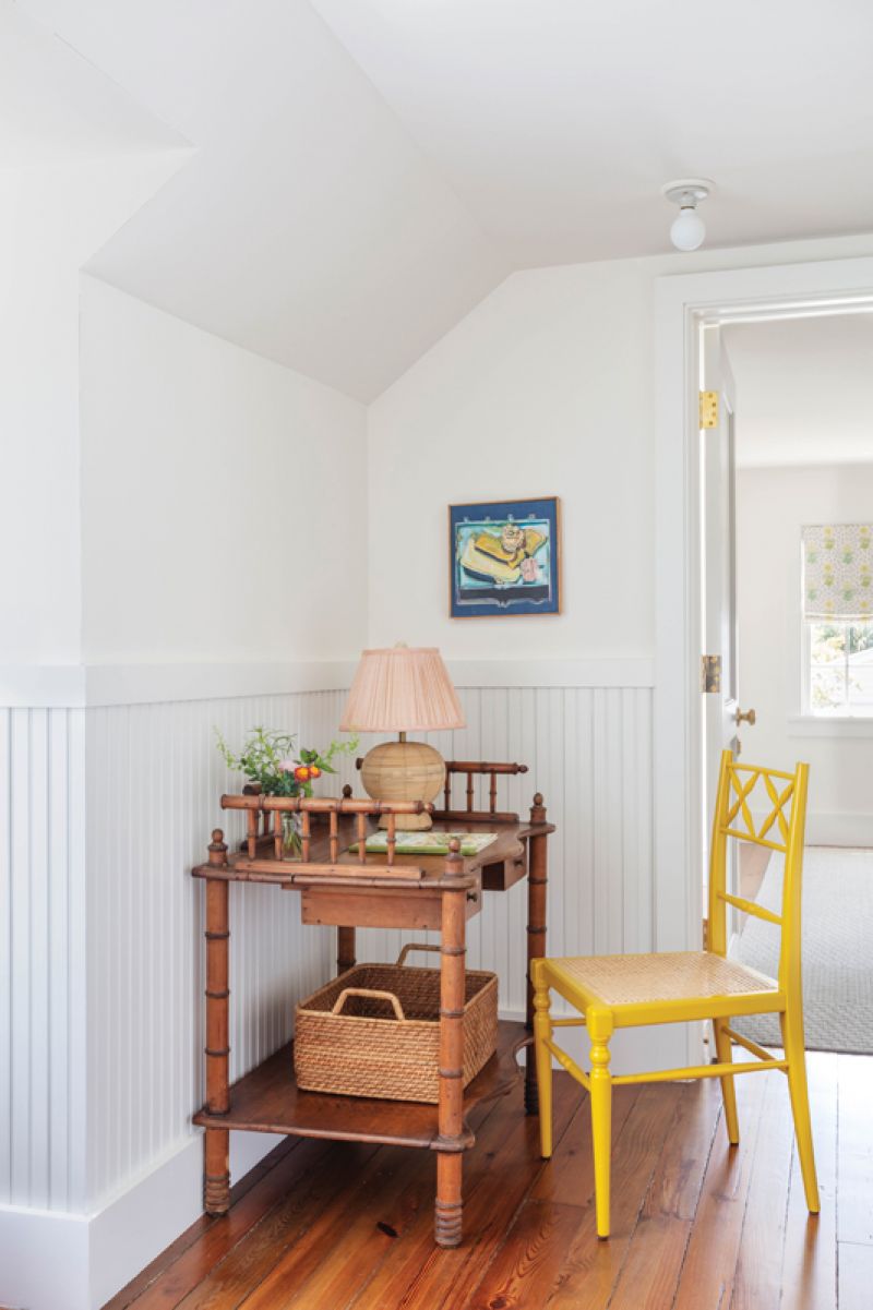 A vintage bamboo desk and a bright yellow Ceraudo chair sit in the hallway near the entrance to a full bath.