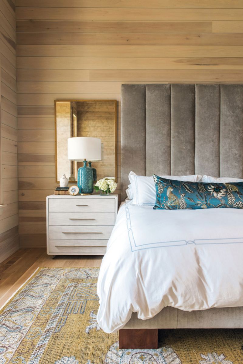 In the primary bedroom, poplar-clad walls, a velvet lumbar pillow (fabric from Ardmore Fabrics), velvet headboard (custom designed by Erickson and upholstered by Powell’s Upholstery), and antiqued glass mirrors layer on the luxe.