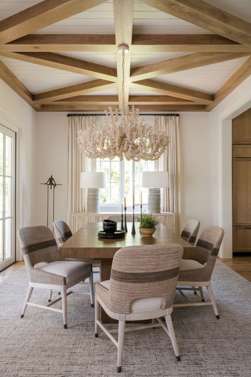 Natural Origins: Wood detailing on the ceiling helps delineate the dining room from the kitchen and living room. Hand-twisted lampakanai rope chairs and a large oak table from Palecek top a wool rug, adding organic interest to the clean space. A showpiece “Seychelles Coco” chandelier from Palecek, with its coral-inspired look, hints at the coastal setting.