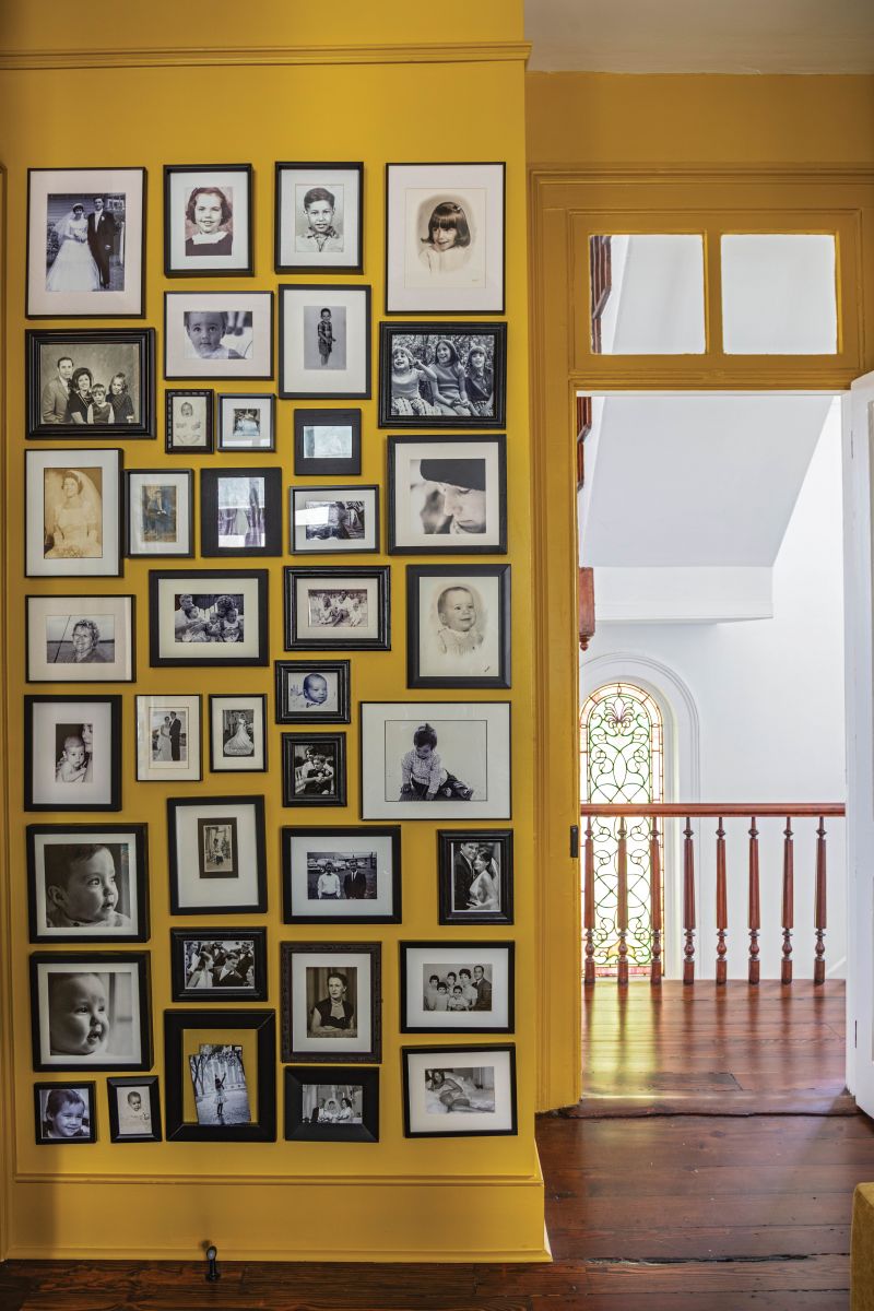 “David is our resident photo archivist,” says Phoebe. “We both grew up with a wall of family photos, so here’s our version.” Built-in shelves painted in the same deep ochre (“Crispy Gold” by Sherwin-Williams) line the facing wall, holding dozens of catalogued photo albums. The stairwell offers a peek of the home’s original stained-glass window.