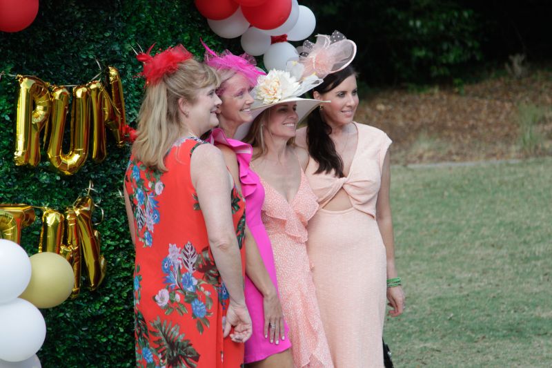 Guests dressed in elegant Derby day attire pose in front of a &quot;Run for the Roses&quot; wall.