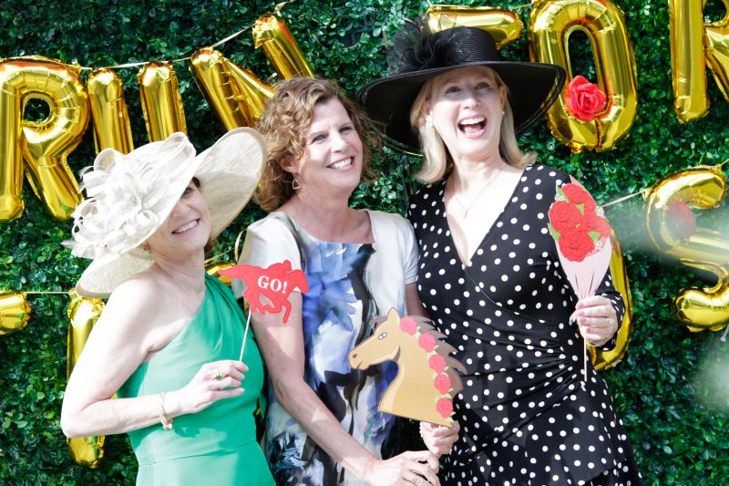 Guests pose in front of a &quot;Run for the Roses&quot; wall with derby props.
